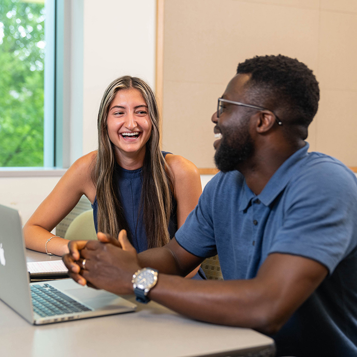 Two students smiling over a laptop